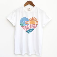 Introducing the Here Comes the Sun T-shirt from Comfort Colors, a retro-style unisex shirt perfect for your next Hawaiian vacation. With its vibrant design and comfortable fit, this shirt is sure to bring some sunshine to your wardrobe. A great gift idea for anyone who loves boho summer style. Summer Cotton T-shirt With Graphic Design, Summer Tops With White Graphic Design, Summer White Print Graphic Tops, Summer White Print Tops With Graphic Design, Summer Graphic Design White Print Tops, White Print Graphic Design Summer Tops, Retro Text Print T-shirt For Beach, Retro White Print Crew Neck T-shirt, Retro Summer Cotton T-shirt