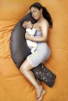 a woman holding a baby in her arms while laying on an orange bed spread with pillows