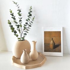 three white vases with green plants in them sitting on a tray next to a painting