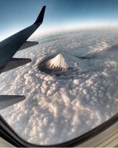 an airplane wing flying over the clouds and a snow capped mountain