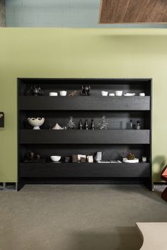 an empty room with green walls and shelves filled with various vases, bowls and other items