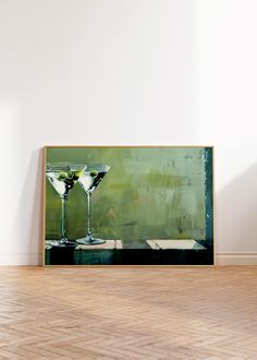 two martini glasses sitting on top of a hard wood floor next to a white wall