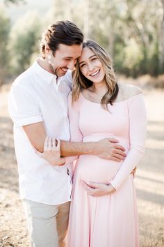 a pregnant couple cuddles in the woods for an outdoor photo session at their family's home