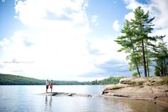 two people standing on the edge of a lake with trees in the background and clouds in the sky