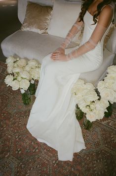 a woman in a white dress sitting on a couch with flowers around her and wearing a veil over her head