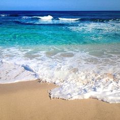 the waves are coming in to the beach with clear blue water and white foamy sand