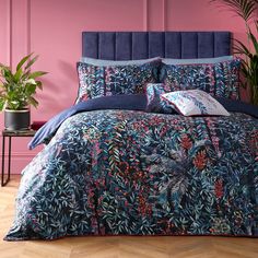 a bed covered in blue and pink comforter next to a potted plant