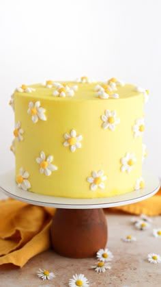 a yellow and white cake with daisies on the top is sitting on a table