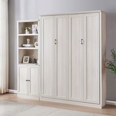 a white bookcase with doors and shelves in a room next to a potted plant