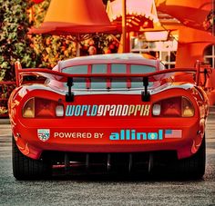 a red sports car is parked in front of some orange lamps and umbrellas at an outdoor event