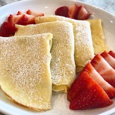 some pancakes and strawberries are on a plate with powdered sugar in the middle