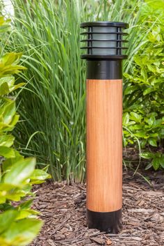 a wooden and black trash can sitting on the ground in front of some bushes with green grass