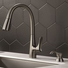 a kitchen faucet that is on top of a sink in front of a tiled wall