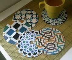 four coasters with designs on them sitting next to a cup