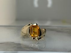 a ring with an orange stone in the center on a glass surface, sitting on top of a table