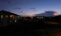 the sky is lit up at night with lights shining on houses and trees in the foreground