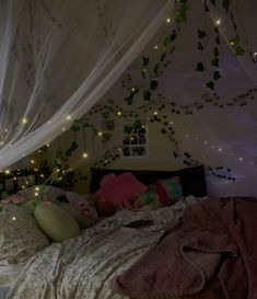 an unmade bed with fairy lights hanging from the ceiling