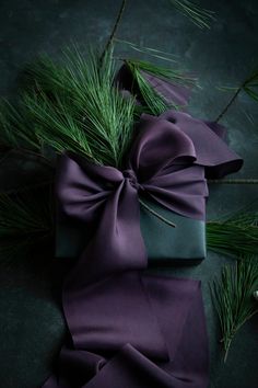 a purple bow tied to a green ribbon on top of a table next to pine branches