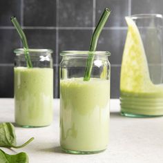 three jars filled with green smoothies on top of a counter