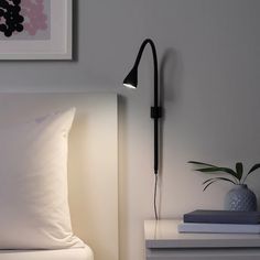 a bed with white sheets and pillows next to a black lamp that is on the wall