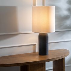 a table lamp sitting on top of a wooden table next to a white wall and window