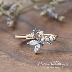 a gold ring with blue and white stones on it sitting on top of a wooden table