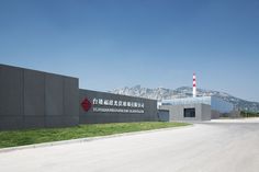 an industrial building with mountains in the background and grass growing on the ground below it