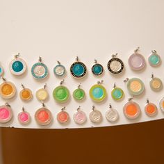 a bunch of different colored round charms on a white surface with a brown wall in the background