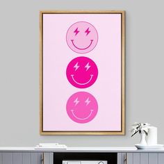 a pink poster with three smiley faces on the wall next to a white table and grey cabinets