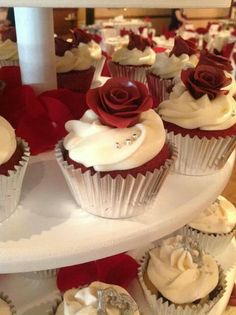 several cupcakes with white frosting and red roses on them are arranged on a three tiered platter