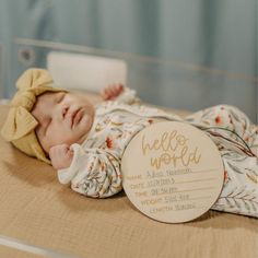 a baby laying on its back next to a wooden plaque with the words hello world written on it