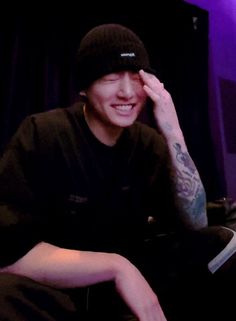 a man with tattoos sitting in front of a purple light and smiling at the camera