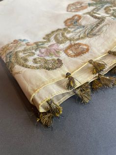 the tassels are attached to the edge of an embroidered fabric with floral designs on it