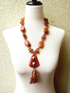 Beautiful vintage inspired, retro 60s, 70s, 80s jewelry - faux amber pendant necklace with golden brown, rich caramel color and golden honey chunky large bead necklace. It is a mix of opaque large chunky stones, each 1 3/8 inches long, and golden bright round beads and chipped stones, with silver tone spacer beads. Unique and alluring pendant with two round balls that spin, and 6 suspended stone chip and bead tassels. Necklace length is 10 inches with 2 inch extension. Secure lobster claw closur 70s Beaded Necklace, Retro Brown Handmade Necklaces, 70s Accessories Jewelry, 70’s Jewelry Necklace, Brown Chunky Necklace, Gold 70s Necklaces, Jewelry Faux, Bead Tassels, Stone Bead Necklace