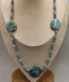 Elevate your style with this stunning handcrafted necklace featuring a beautiful combination of turquoise stones, crystals and silver accents. The centerpiece includes three large , polished turquoise stones, each showcasing unique patterns and vibrant hue. Interspersed between the turquoise are delicate light blue crystal beads and shimmering silver spacer beads, adding touch of elegance and contrast. The necklace is designed to lay gracefully around the neck, making it a perfect accessory for Silver Amazonite Necklace With Gemstone Beads, Bohemian Silver Amazonite Necklaces, Silver Amazonite Necklace With Natural Stones, Adjustable Turquoise Stone Necklace, Adjustable Turquoise Stone Necklaces, Elegant Turquoise Agate Beaded Necklaces, Artisan Turquoise Beaded Necklaces With Stones, Silver Chrysocolla Jewelry With Gemstone Beads, Turquoise Chrysocolla Stone Necklaces