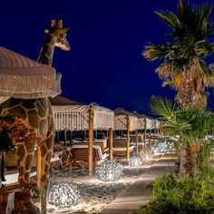 a giraffe statue sitting on top of a sandy beach next to palm trees