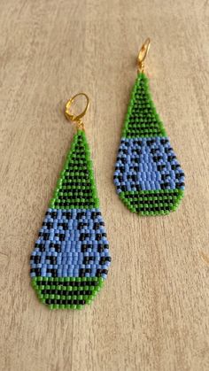 a pair of blue and green beaded earrings sitting on top of a wooden table