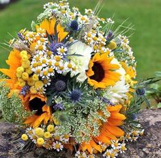 a bouquet of sunflowers and other flowers is sitting on top of a rock