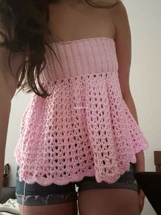 a woman in shorts is wearing a pink crochet top and has her back turned to the camera