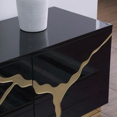 a black and gold sideboard with a white vase on it's end table