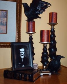 a black bird sitting on top of a table next to two candles and a framed photo