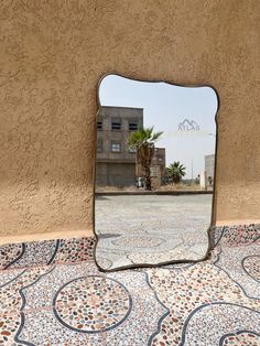 a large mirror sitting on top of a floor next to a wall with a building in the background