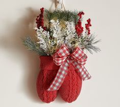 a pair of red mittens hanging on a wall with flowers in it and a plaid bow