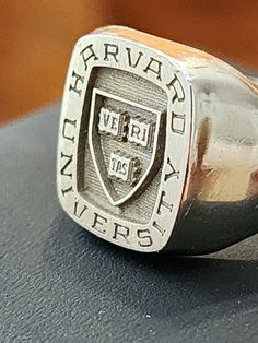 GENUINE HARVARD UNIVERSITY 18K WHITE GOLD SIGNET SCHOOL RING SIZE 9.5 - 10. ITS APPRXIMATELY 11.9 GRAM OF SOLID 18K GOLD. (No stone weight) This is my personal graduate school signet ring from Harvard University, Faculty of Arts and Science. It's Josten brand, 18k solid white gold, and a "hand engraved" signet ring. It is not laser engraved like today's typical ring. In fact, this handmade design was discontinued, and now Josten makes easy laser-engraved signet rings. My name is lightly engraved Engraved Signet Ring, Arts And Science, School Rings, College Education, Signet Rings, Harvard University, Ring Pictures, Graduate School, Book Store