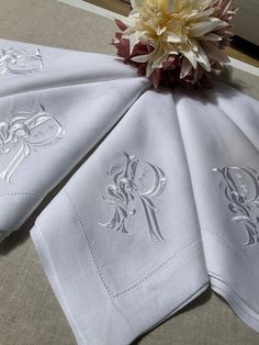 three white napkins with monogrammed designs on them and a flower in the middle