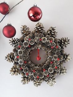 a christmas wreath with pine cones and ornaments hanging on a wall next to two red baubles