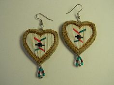 two heart shaped earrings with beads hanging from the side on a white surface, one is made out of woven material