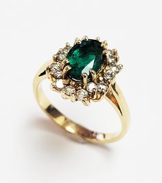 an emerald and diamond cluster ring on a white surface, with the center stone surrounded by smaller diamonds