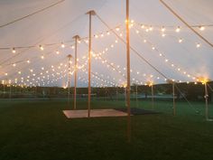 a large tent with lights on the ceiling and some grass in front of it at night