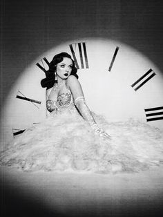 a black and white photo of a woman in a ball gown sitting on a clock